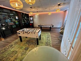 Una stanza con un tavolo da calcio, un biliardo e una libreria con diversi oggetti.
