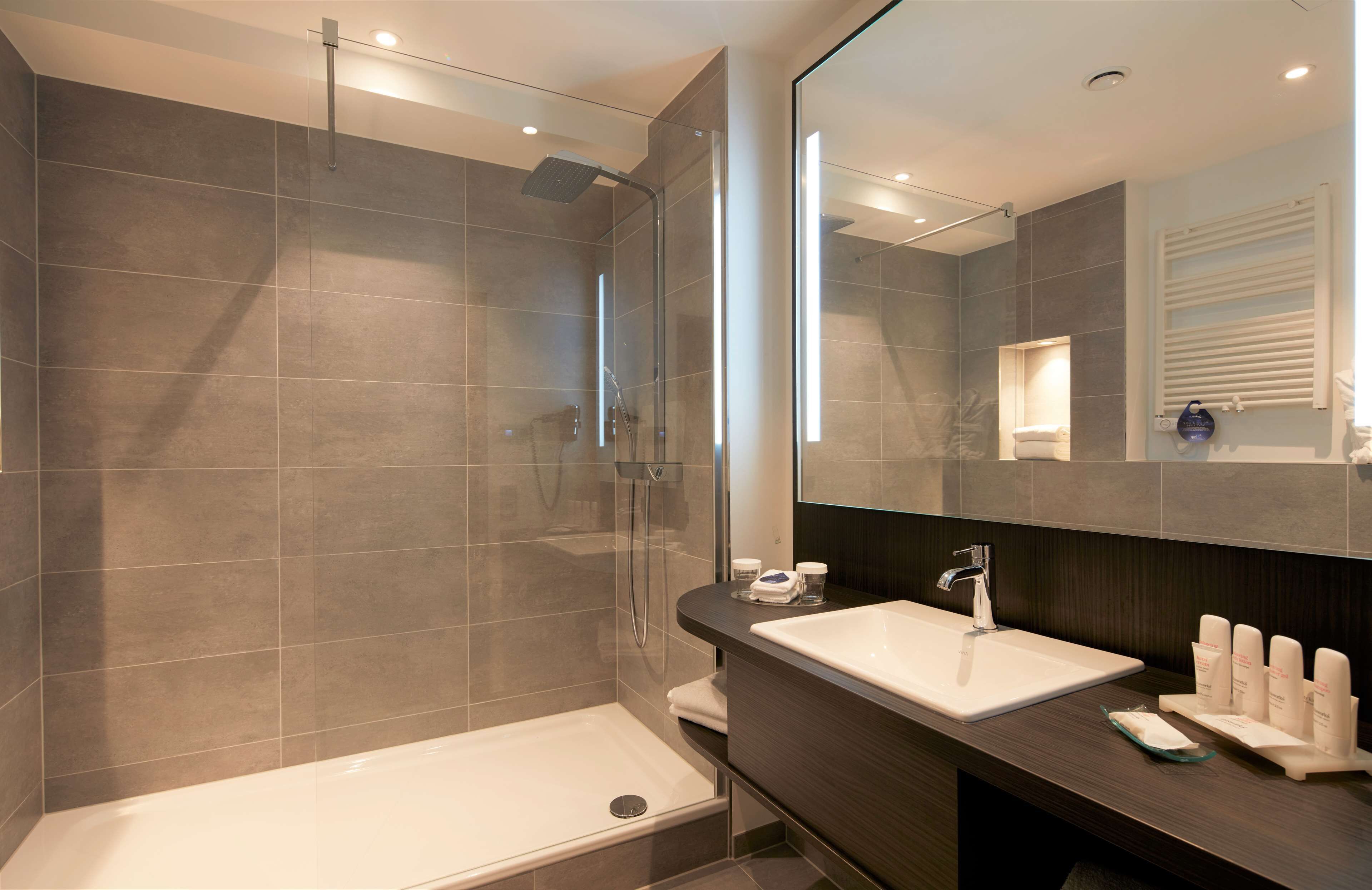 Un baño moderno con ducha envuelta en vidrio, una bañera independiente y un tocador con un espejo grande y encimera.