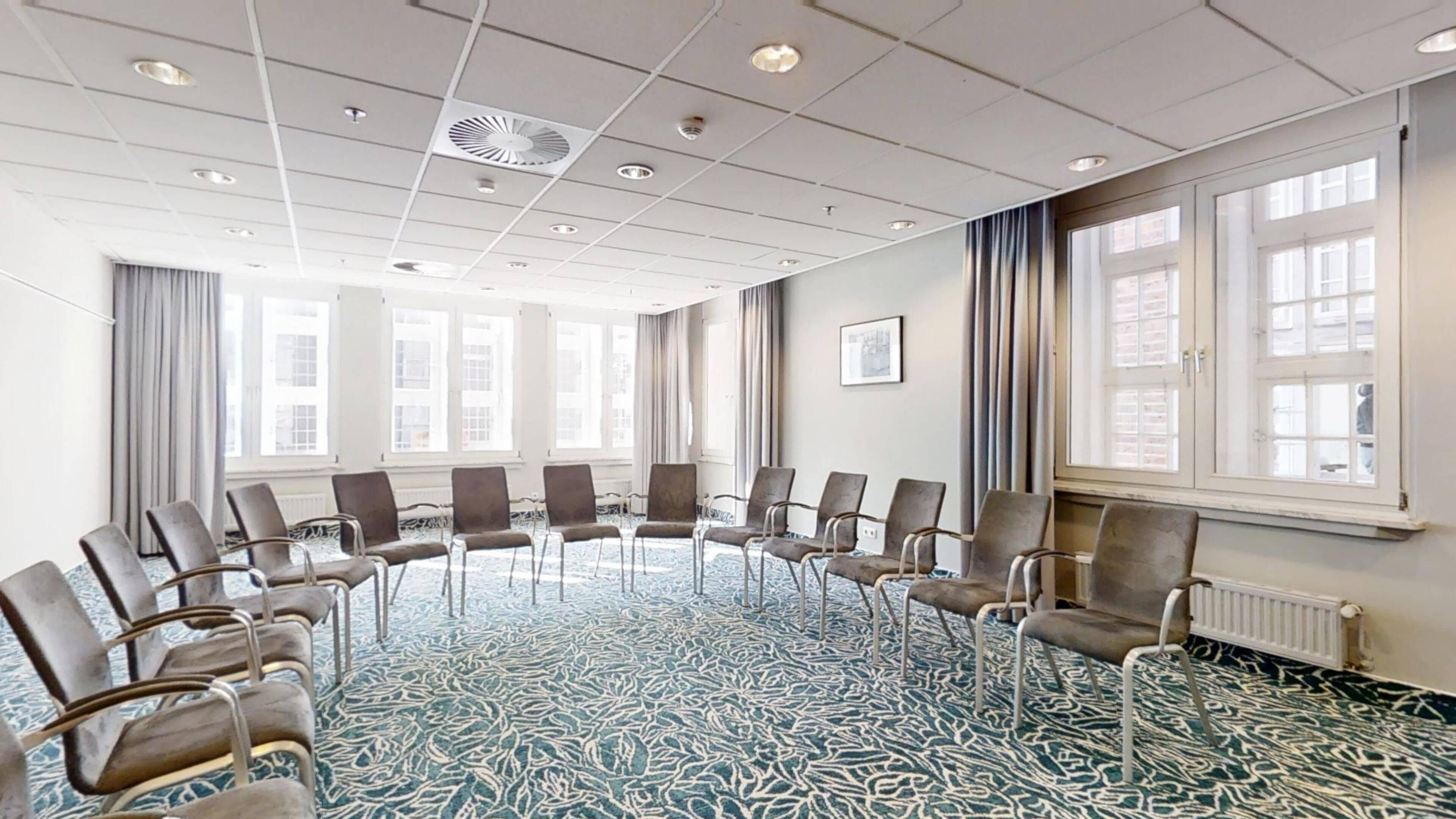 Un salón de conferencias con alfombra estampada, filas de sillas, ventanas amplias e iluminación empotrada en el techo.