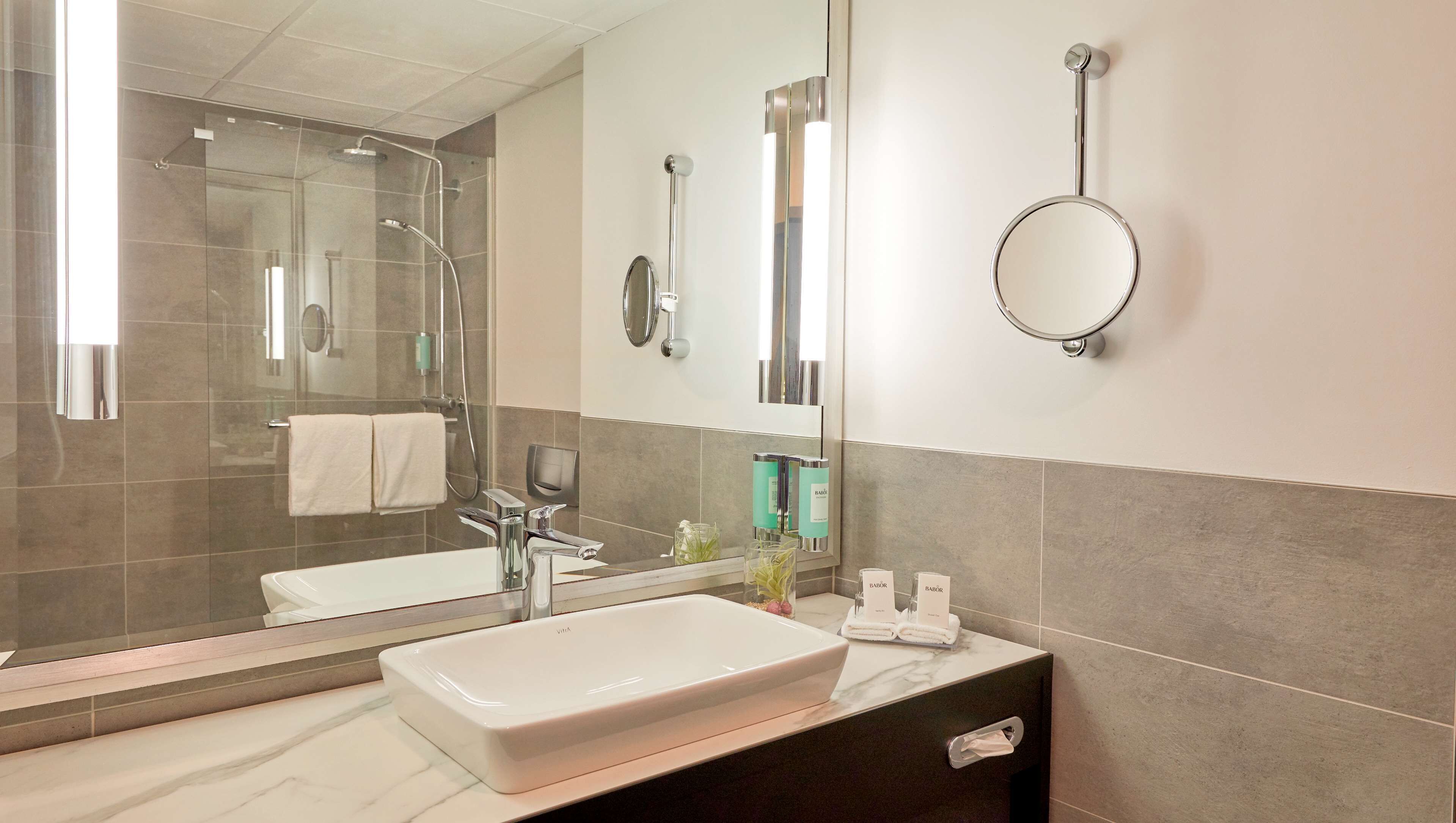 Un baño moderno con un espejo grande, un lavabo y una zona de ducha.