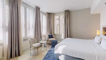 A hotel room with a large bed, a chair, a small table, and curtains.