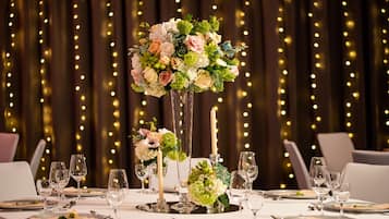 A table set for a formal dining occasion with a floral centerpiece, candles, and a dimly lit background with string lights.