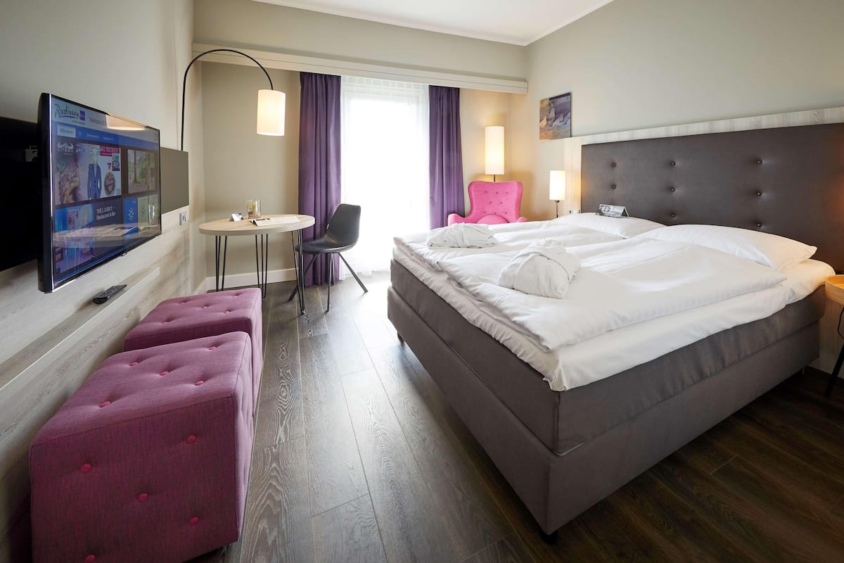 A hotel room with a bed, a desk, a chair, a TV, and a window with curtains.