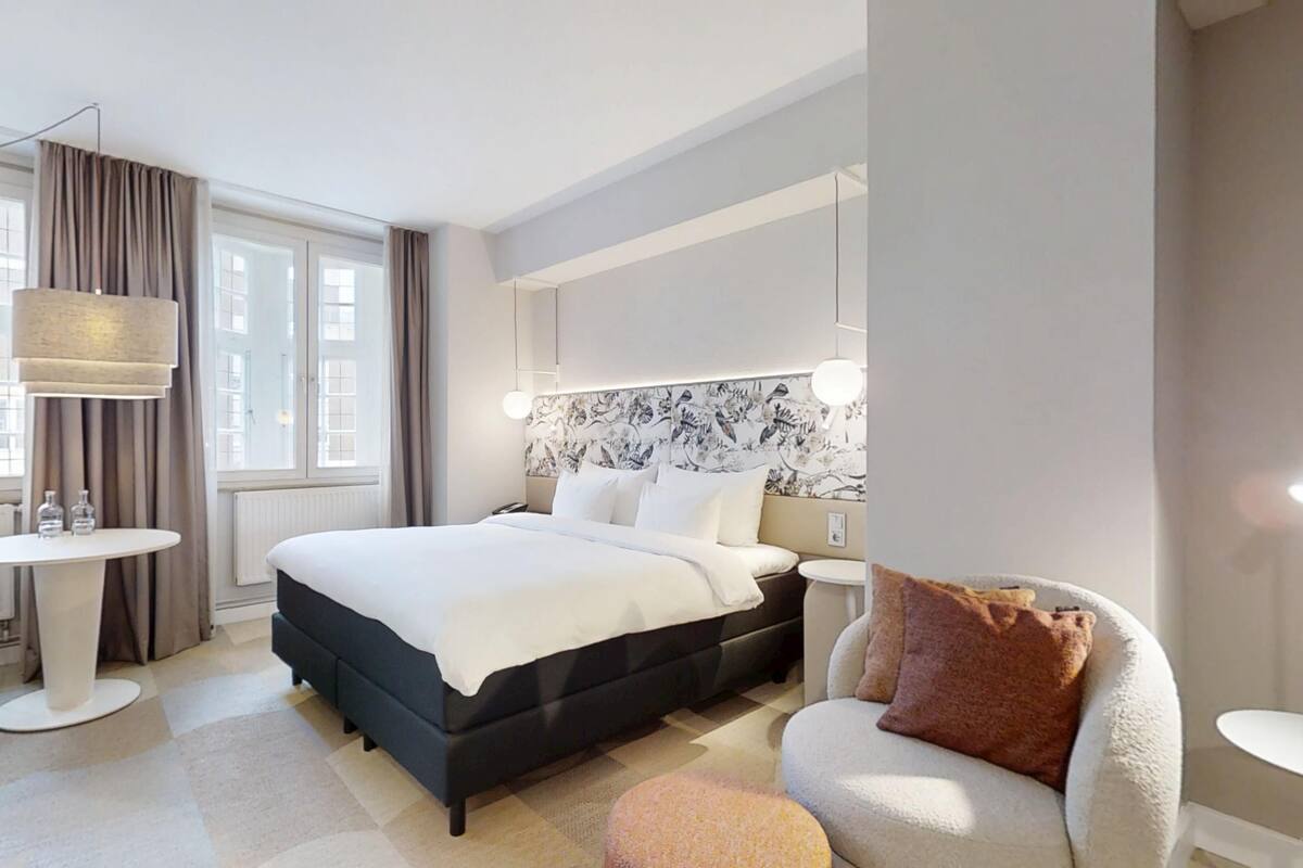 A modern hotel room with a large bed, a desk, a chair, and a sofa.