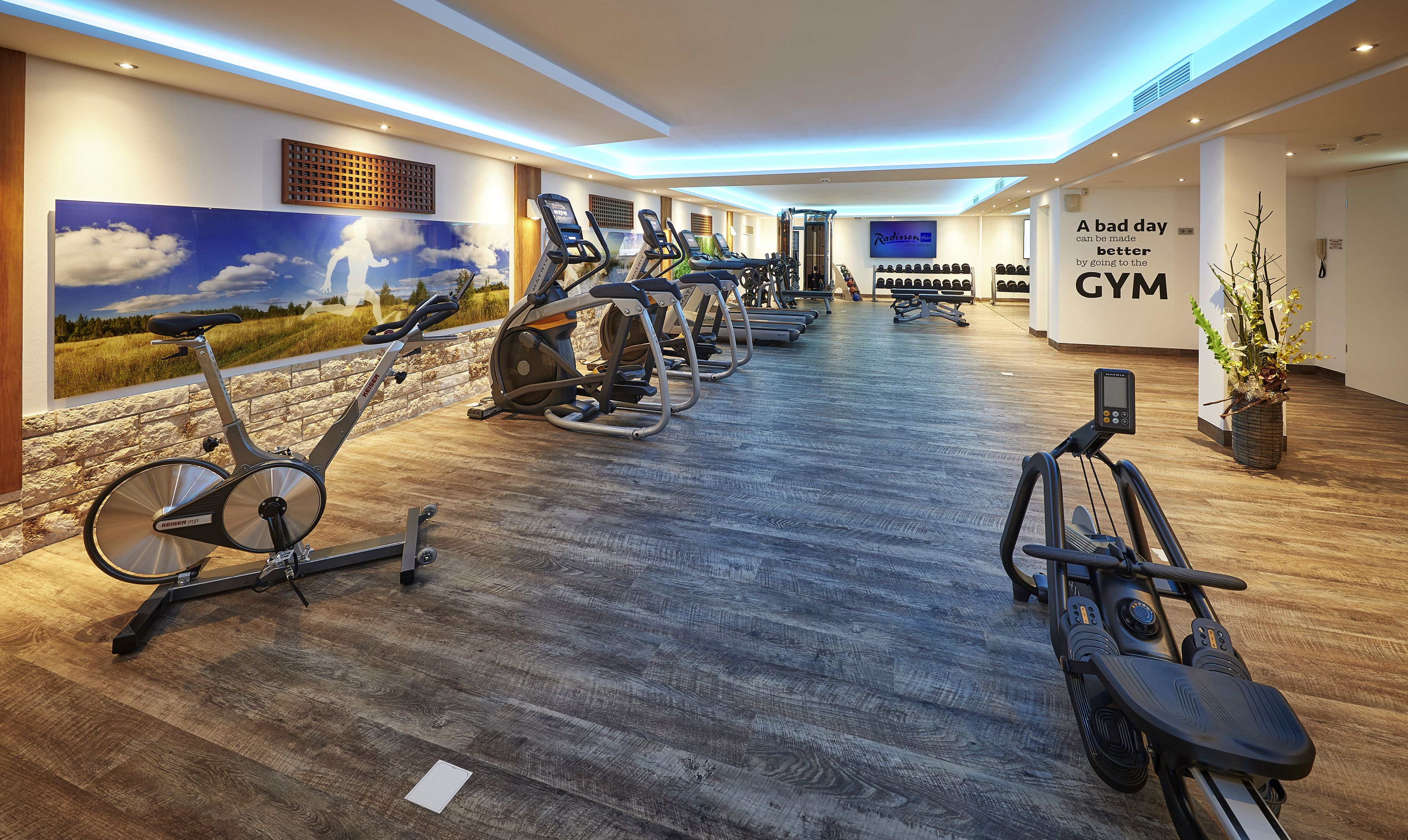 Un gimnasio con bicicletas estáticas, cintas de correr y una pared con una frase motivacional.