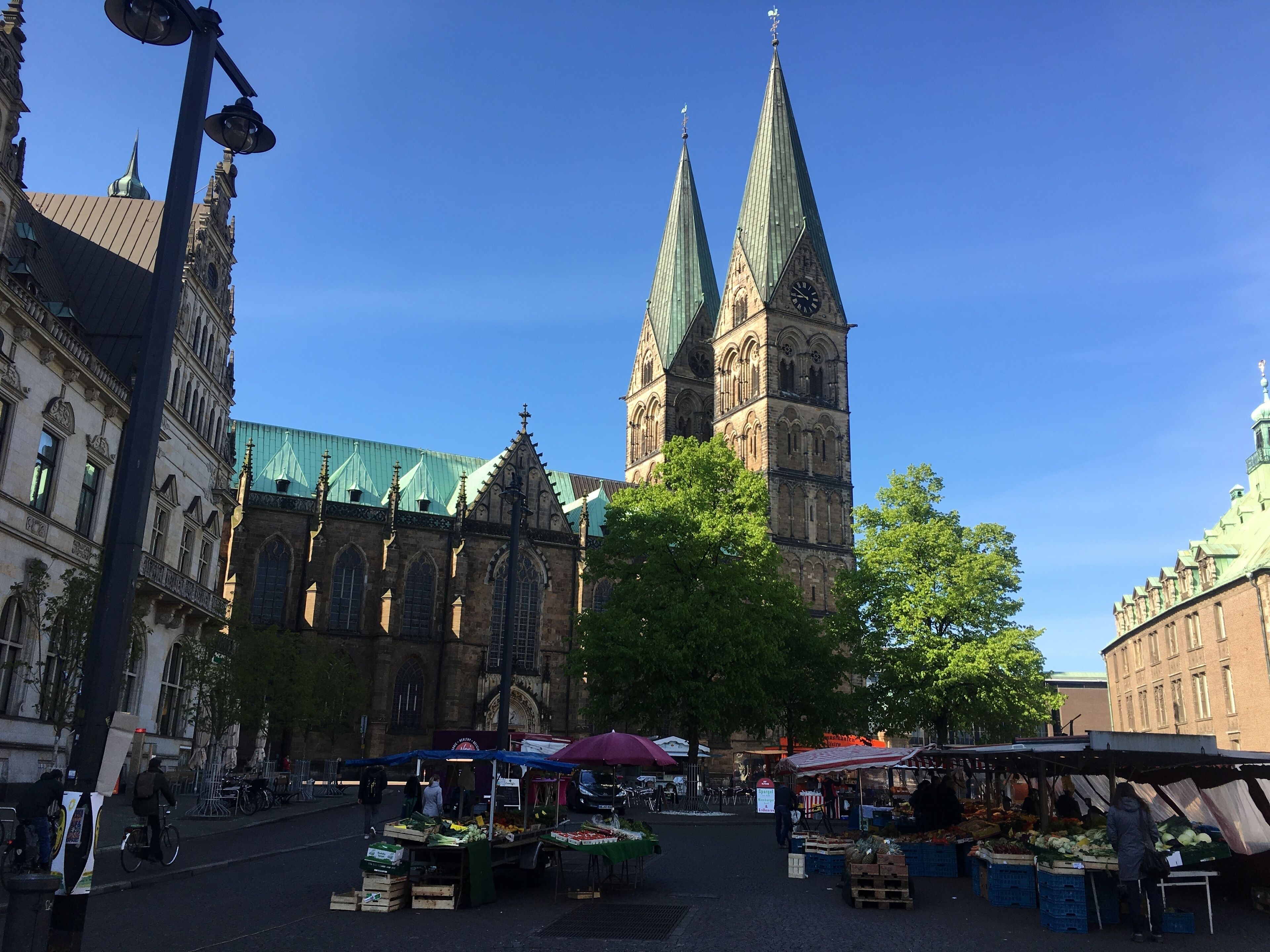 A historic market square with stalls, a prominent church with twin spires, and a clear blue sky.
