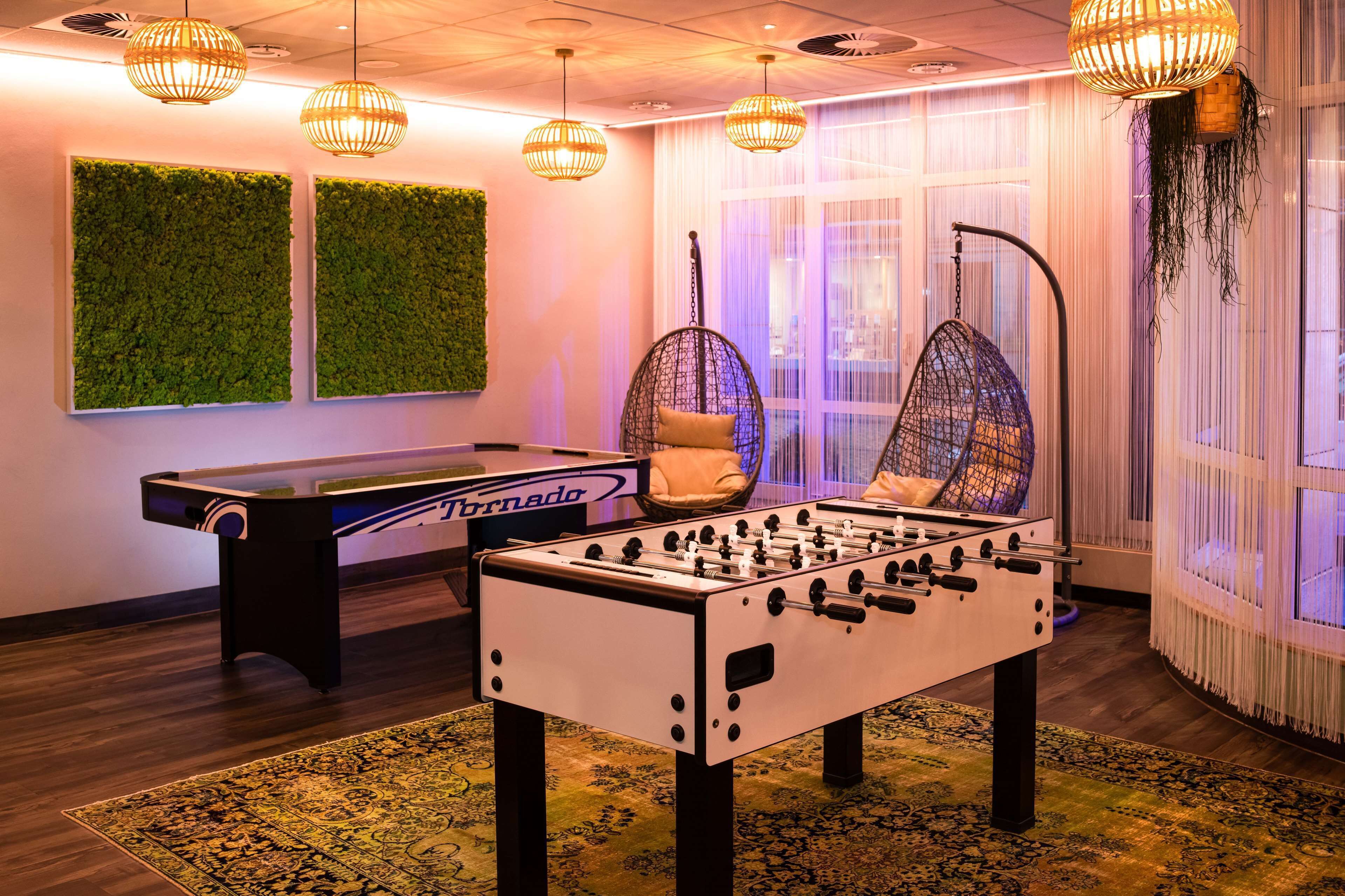 A foosball table in a room with a green wall, hanging lights, and a large window with curtains.