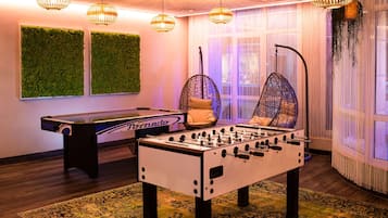 A foosball table in a room with a green wall, hanging lights, and a large window with curtains.