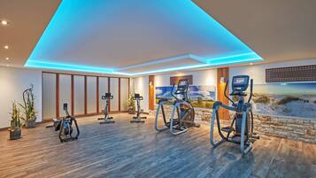 A modern gym with exercise equipment, wooden flooring, and a scenic wall mural.