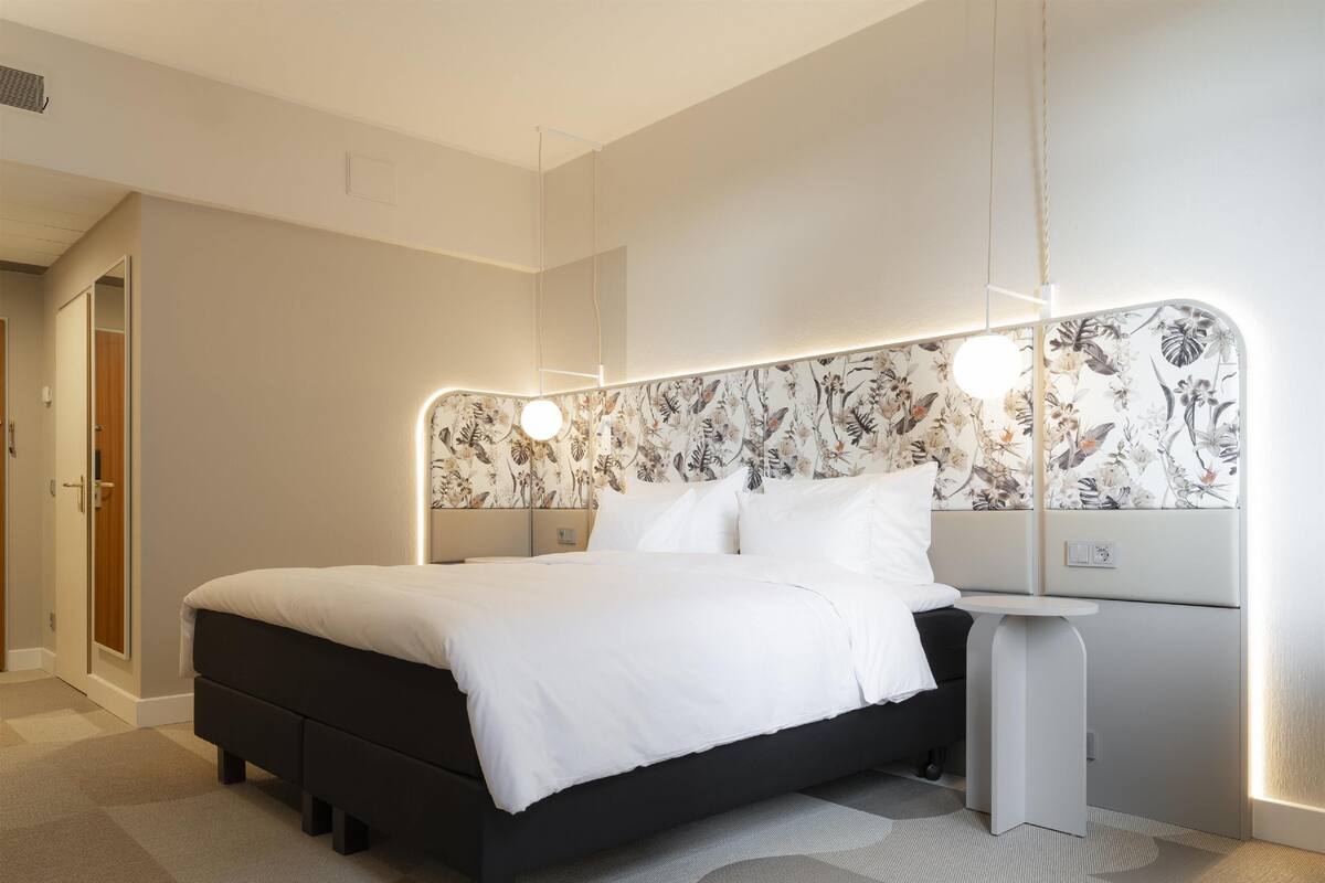 A modern bedroom with a black bed, white bedding, and a floral-patterned headboard.