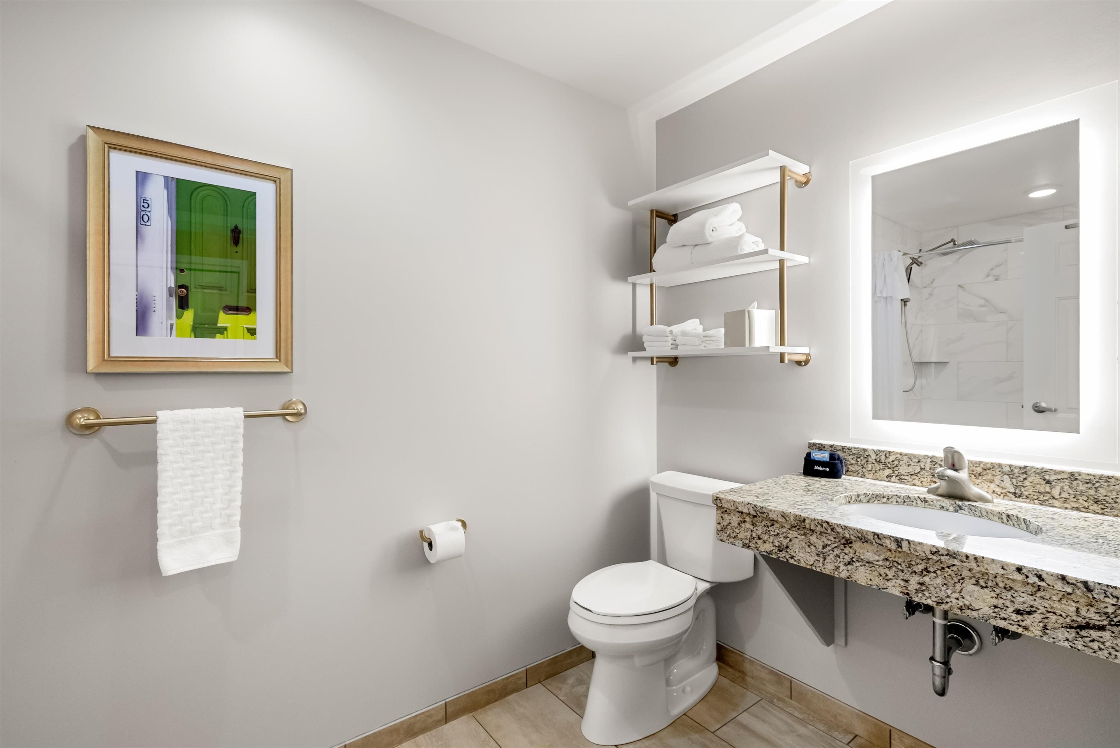 A modern bathroom with a toilet, a sink with a marble countertop, a towel rack with a white towel, and a framed picture on the wall.