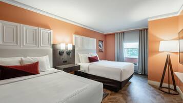 Een hotelkamer met twee bedden, een houten visgraatvloer, een raam met gordijnen en een wandlamp.