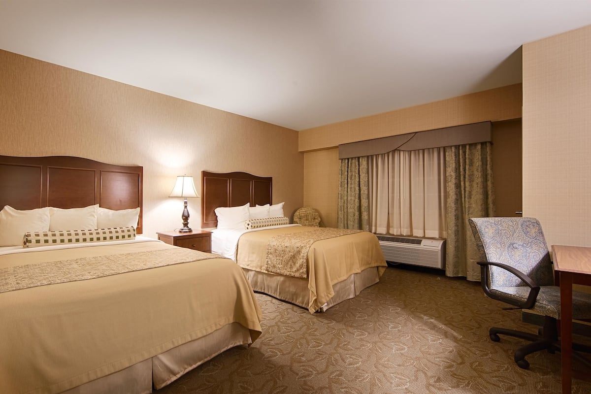 A hotel room with two beds, a desk, a chair, and a window with curtains.