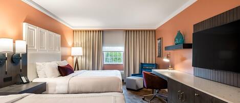 A hotel room with two beds, a desk, a TV, and a window with curtains.