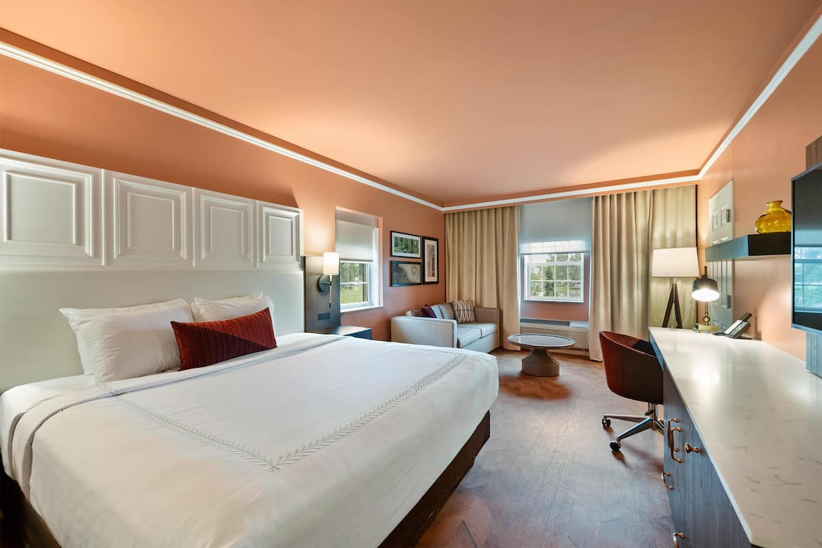 A hotel room with a large bed, a desk, a chair, and a window with curtains.