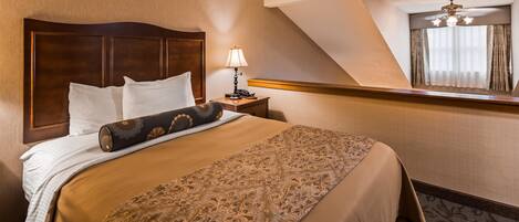 A hotel room with a large bed, a nightstand with a lamp, a headboard, and a window with curtains.