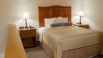 A hotel room with a wooden headboard, a bed with a beige bedspread, two bedside tables with lamps, a nightstand, and a wooden bench.