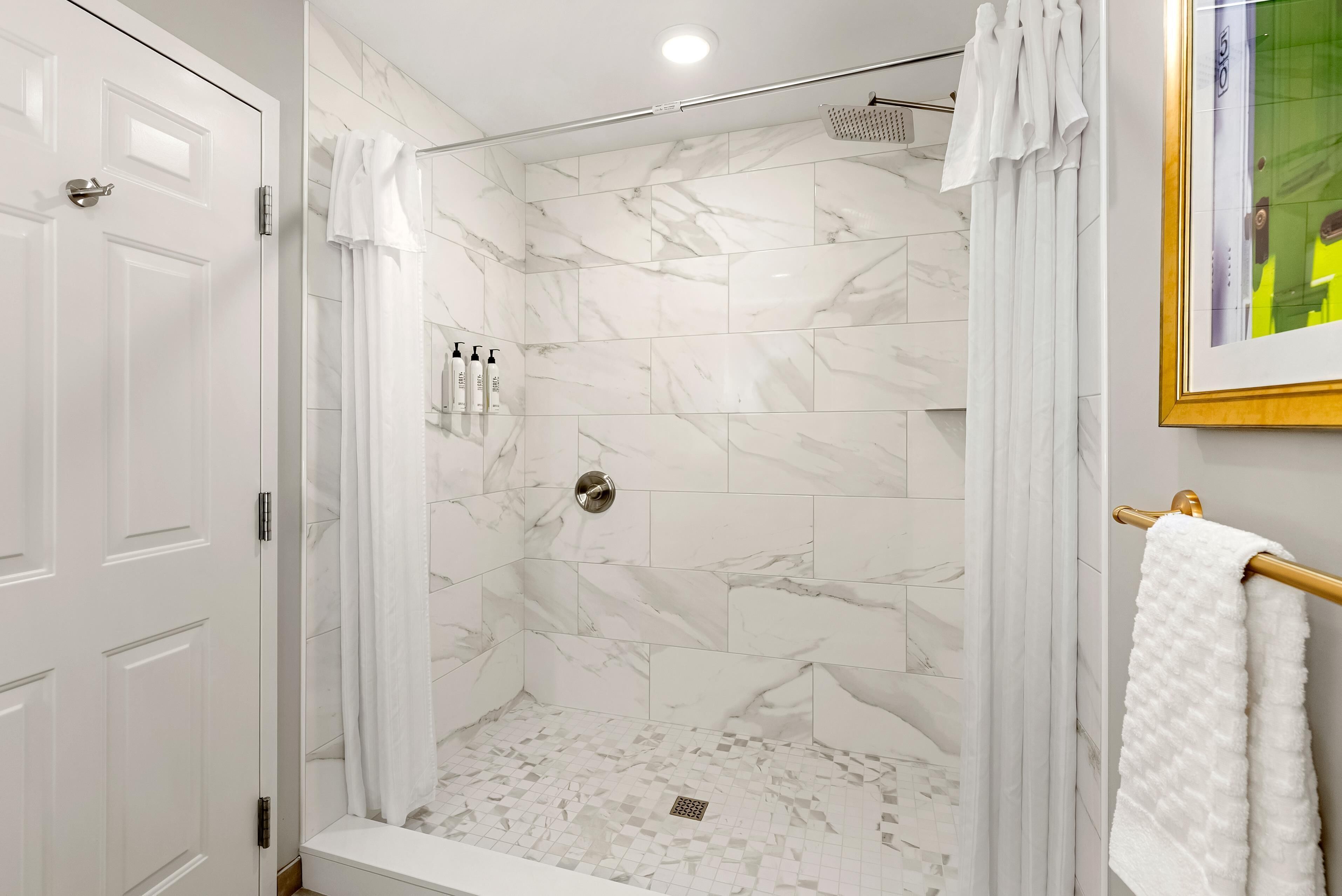 A walk-in shower with white marble tiles, a glass door, and a towel rack.