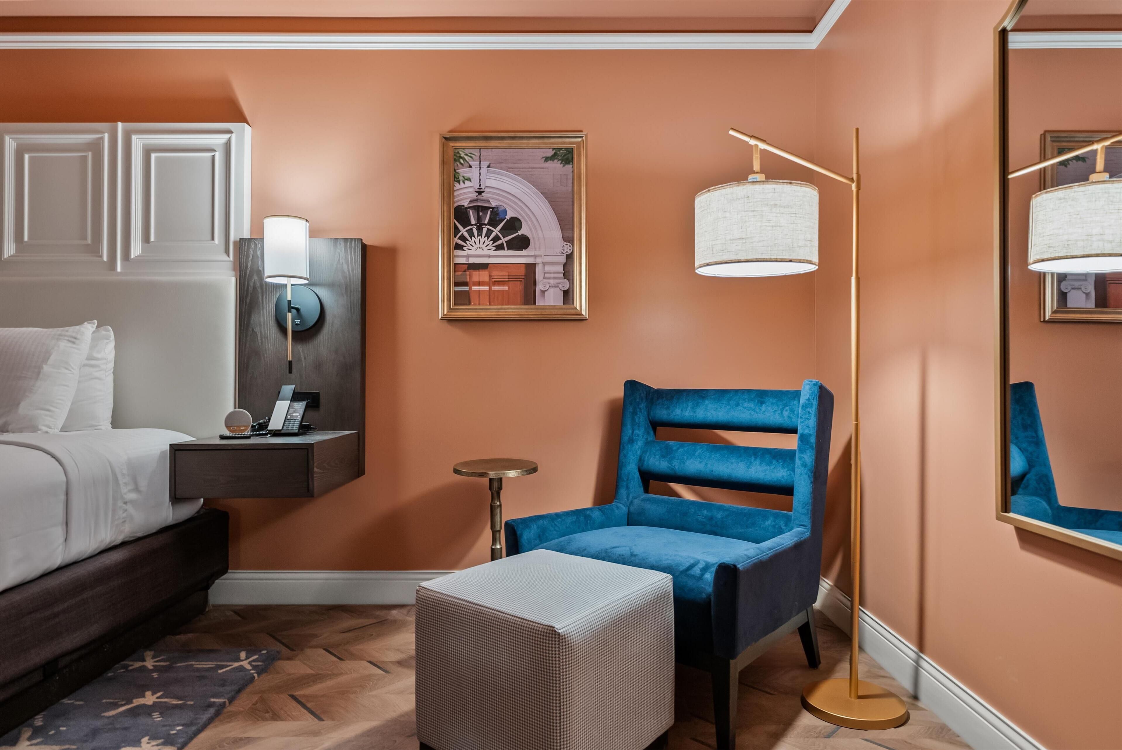 A bedroom with a bed, bedside table, lamp, framed artwork, and a blue chair.