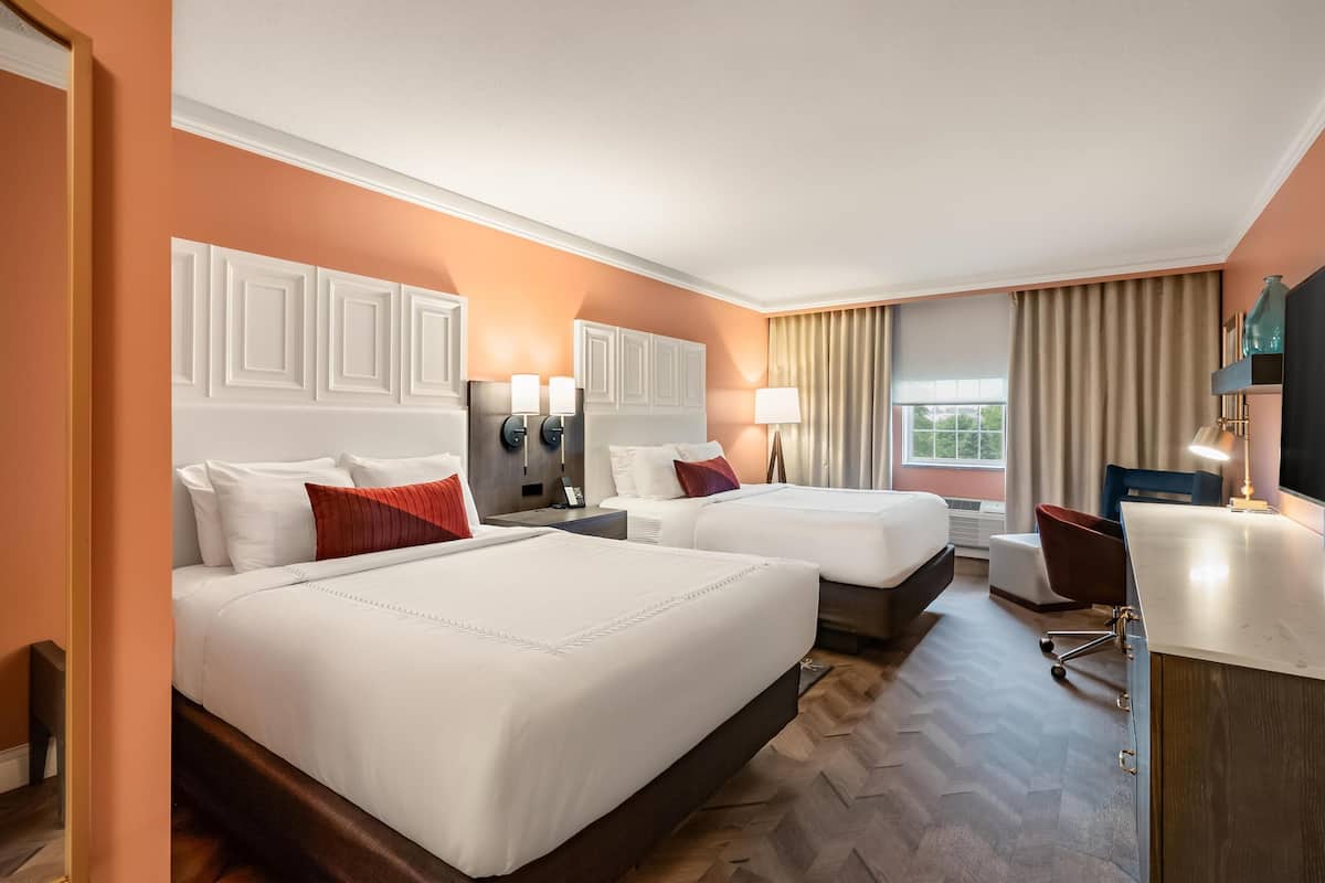 A hotel room with two beds, a desk, a chair, and a window with curtains.