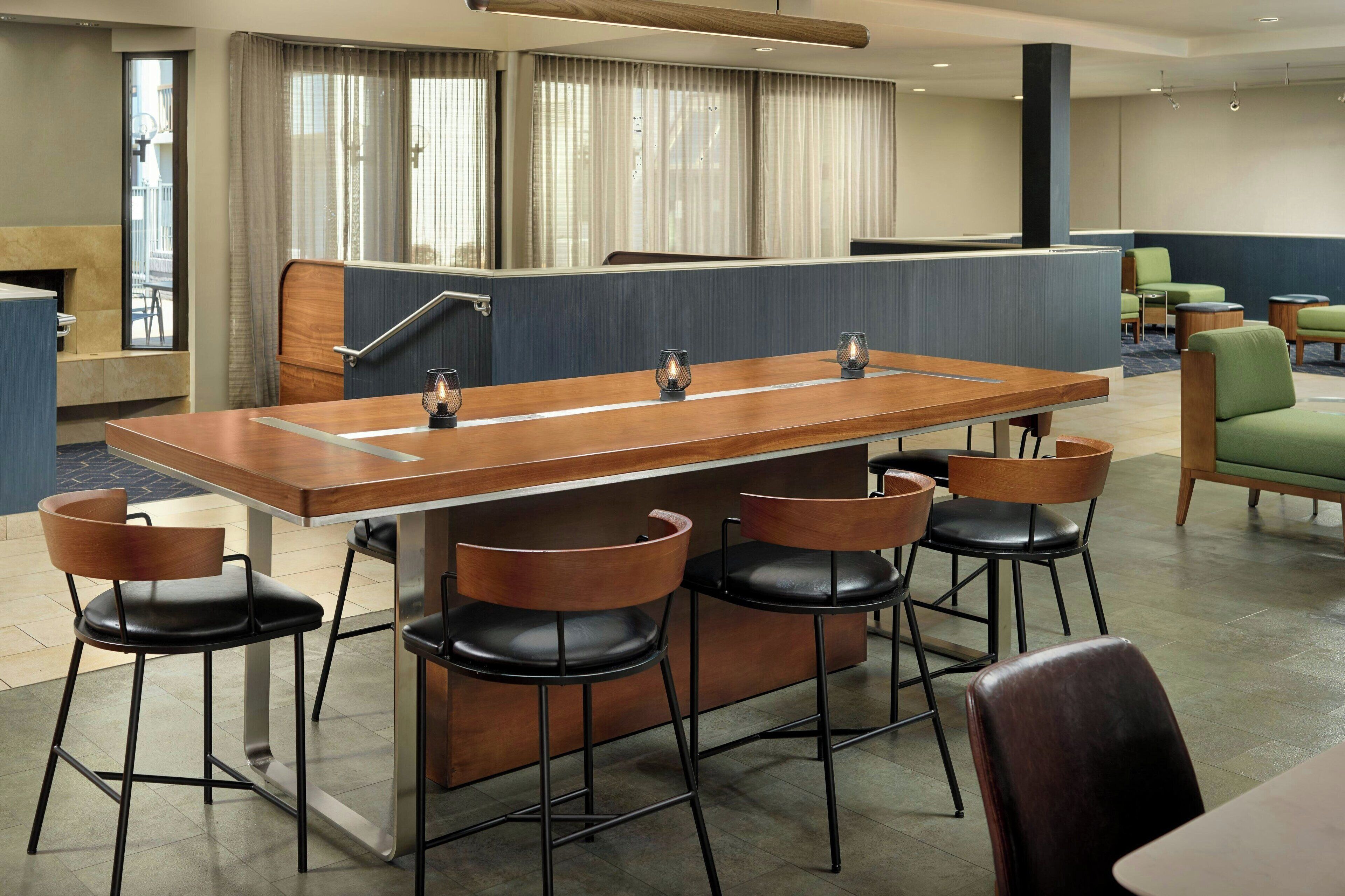 En moderne hotellobby med en lang træreception, sorte læderbarstole og grønne polstrede stole.
