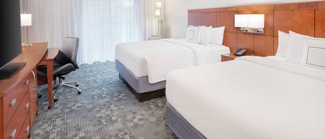 A hotel room with two beds, a desk with a chair, a TV, and a large window with curtains.