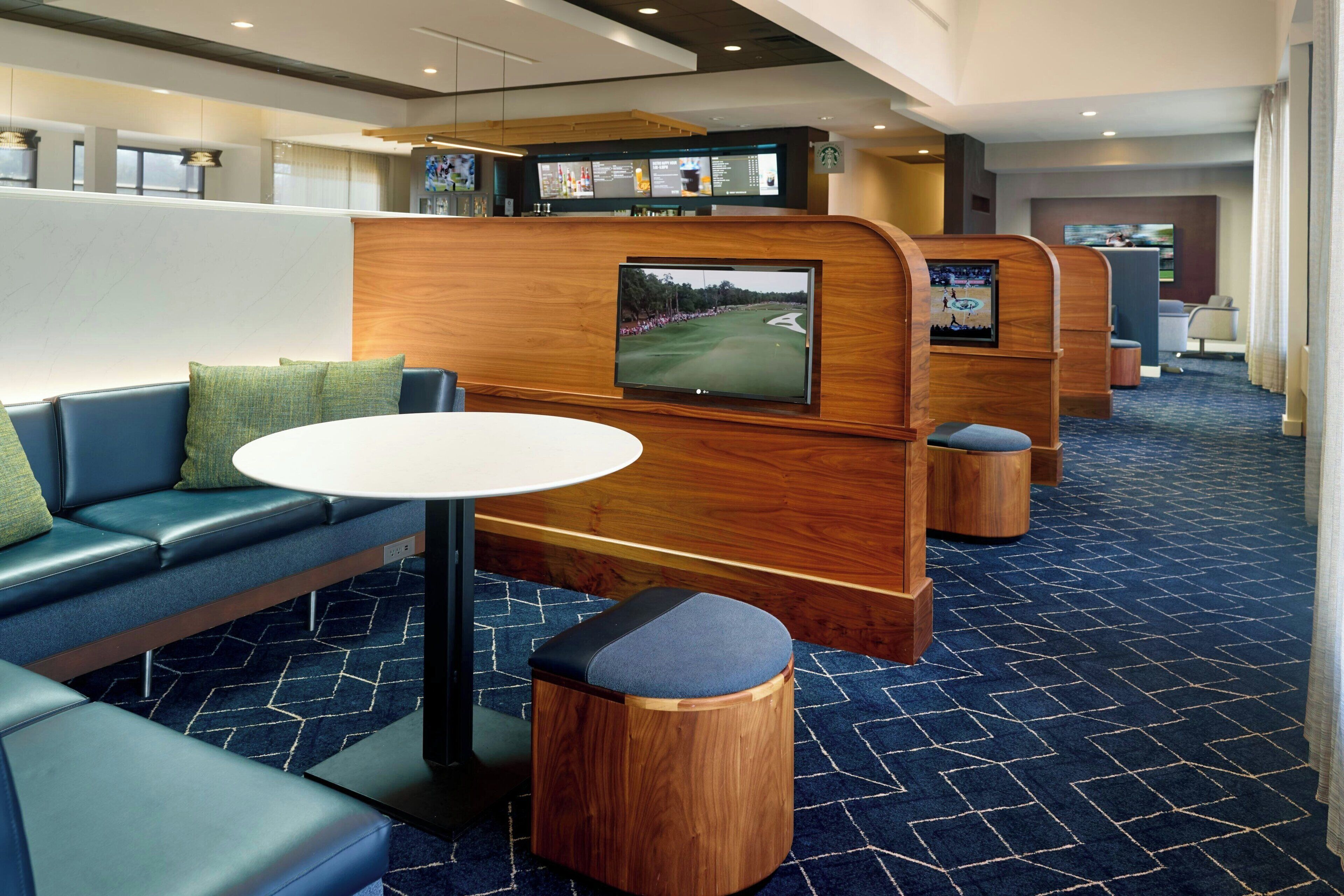 Un moderno hall de hotel con zonas de estar, una recepción y una pantalla grande que muestra un campo de golf.