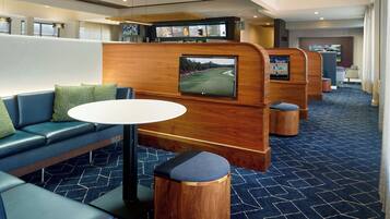 Un moderno hall de hotel con zonas de estar, una recepción y una pantalla grande que muestra un campo de golf.