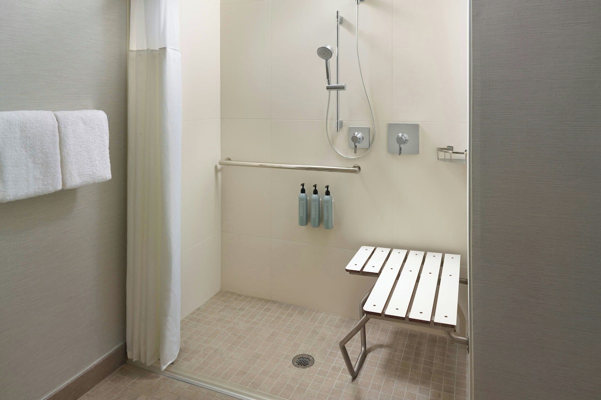 Een compacte, moderne badkamer met een douche, handgrepen en een zitje.