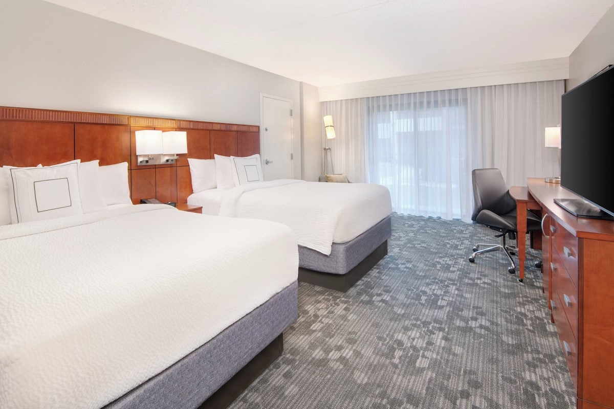 Een hotelkamer met twee bedden, een bureau, een stoel en een televisie.