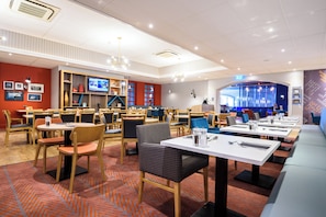 A modern restaurant with multiple dining areas, a television screen, and a variety of seating options. - Holiday Inn Portsmouth by IHG (Portsmouth)