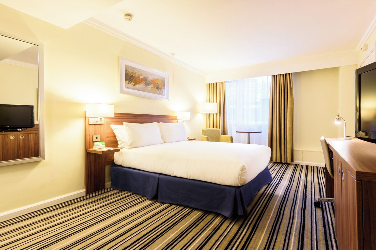 A hotel room with a large bed, a flat-screen TV, a desk with a lamp, and a painting on the wall.
