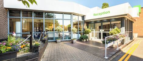 A reception area with a glass facade, outdoor seating, and potted plants.
