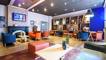 A modern lounge area with seating, a fireplace, and a television screen displaying news.