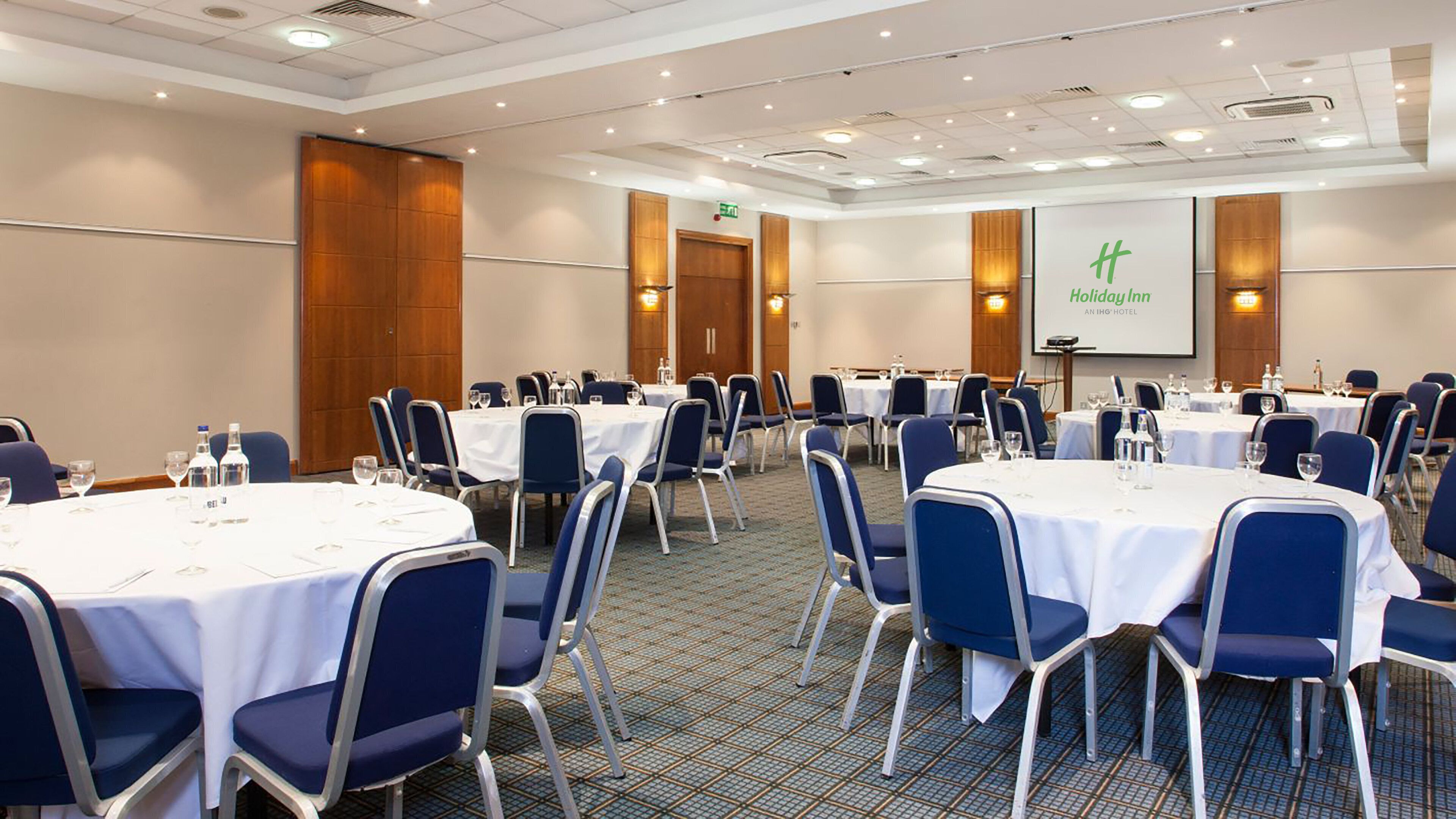 A conference room with round tables, chairs, and a presentation screen.