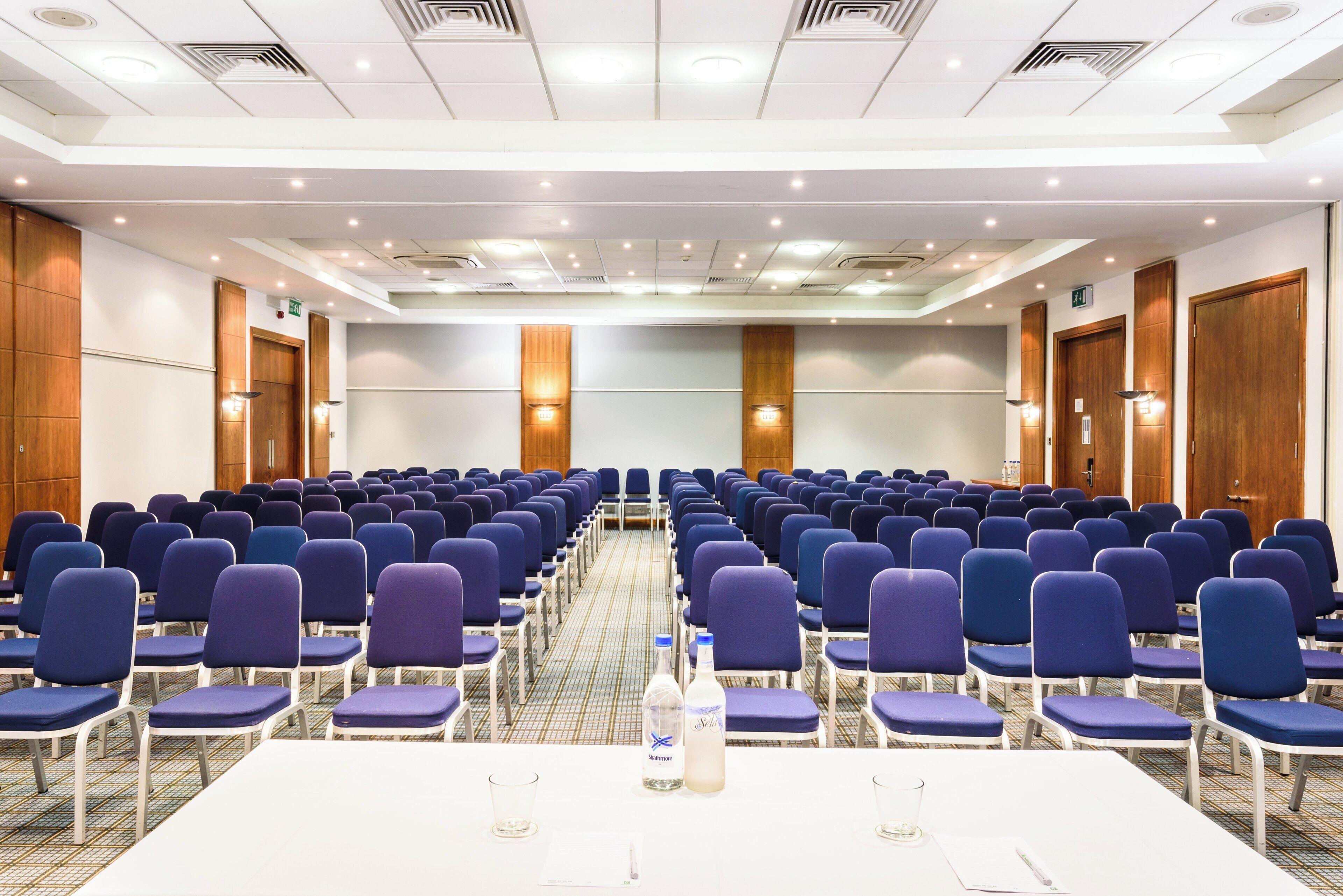Un salón de conferencias con filas de sillas, una mesa larga y un atril.