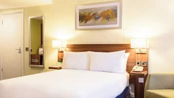 Habitación de hotel con una cama grande, dos lámparas de noche, un cabecero de madera, un cuadro en la pared, un teléfono junto a la cama y una silla.
