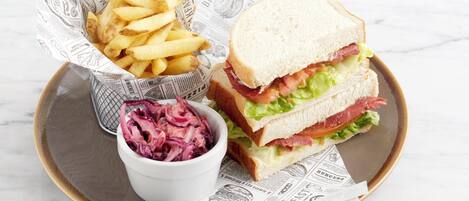 Una bandeja con un sándwich, papas fritas y ensalada de col sobre una superficie de mármol.