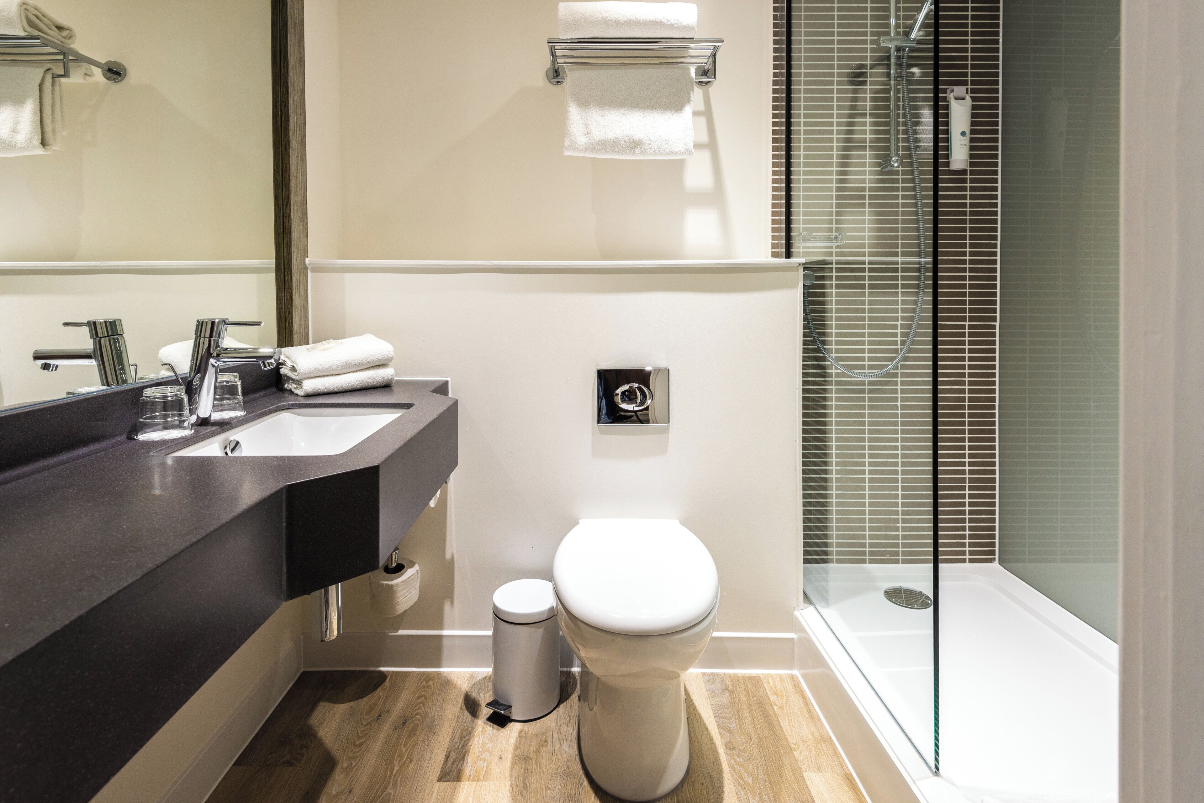 Un baño moderno con encimera negra, inodoro blanco y cabina de ducha de cristal.