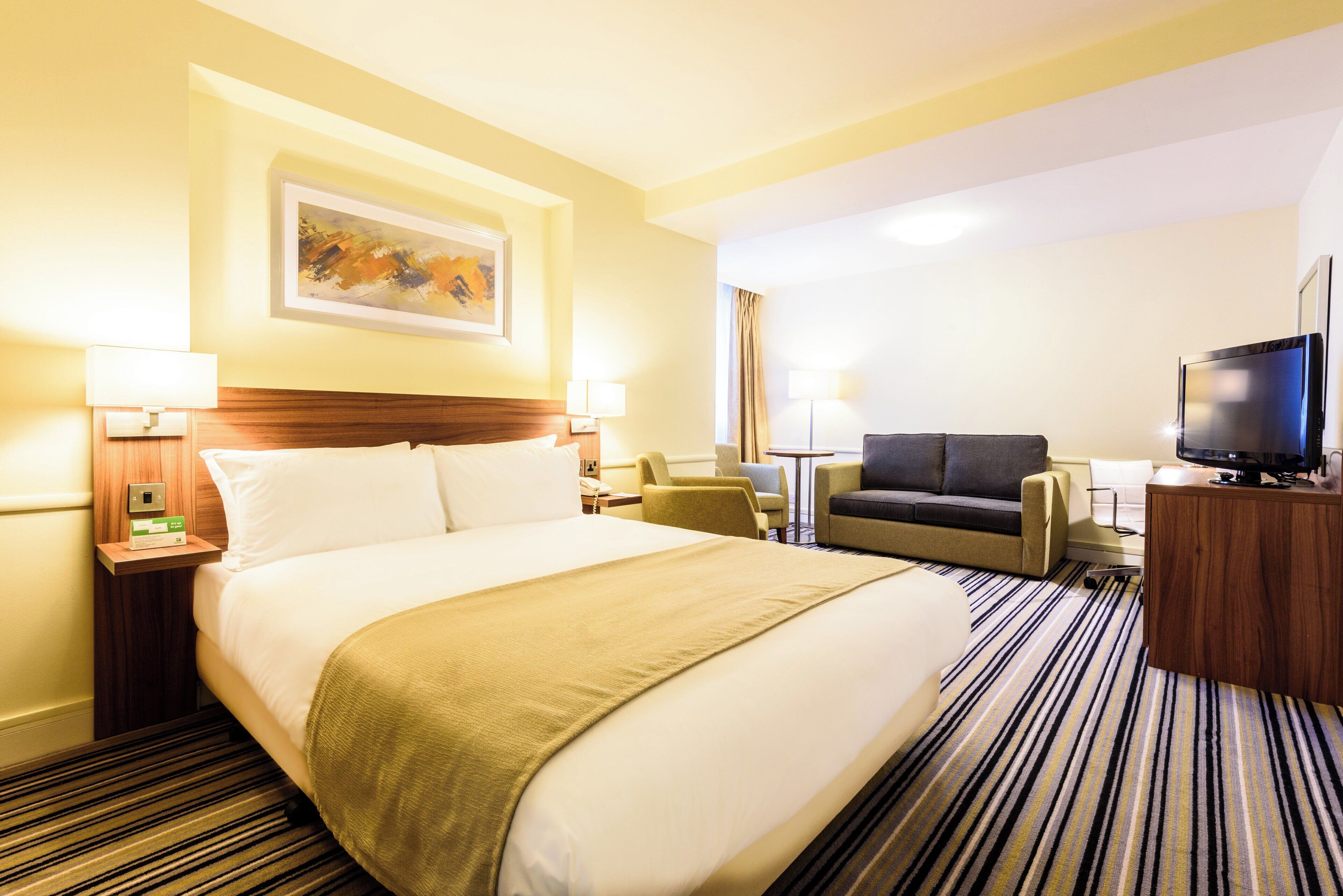 A hotel room with a large bed, a sofa, a television, and a painting on the wall.