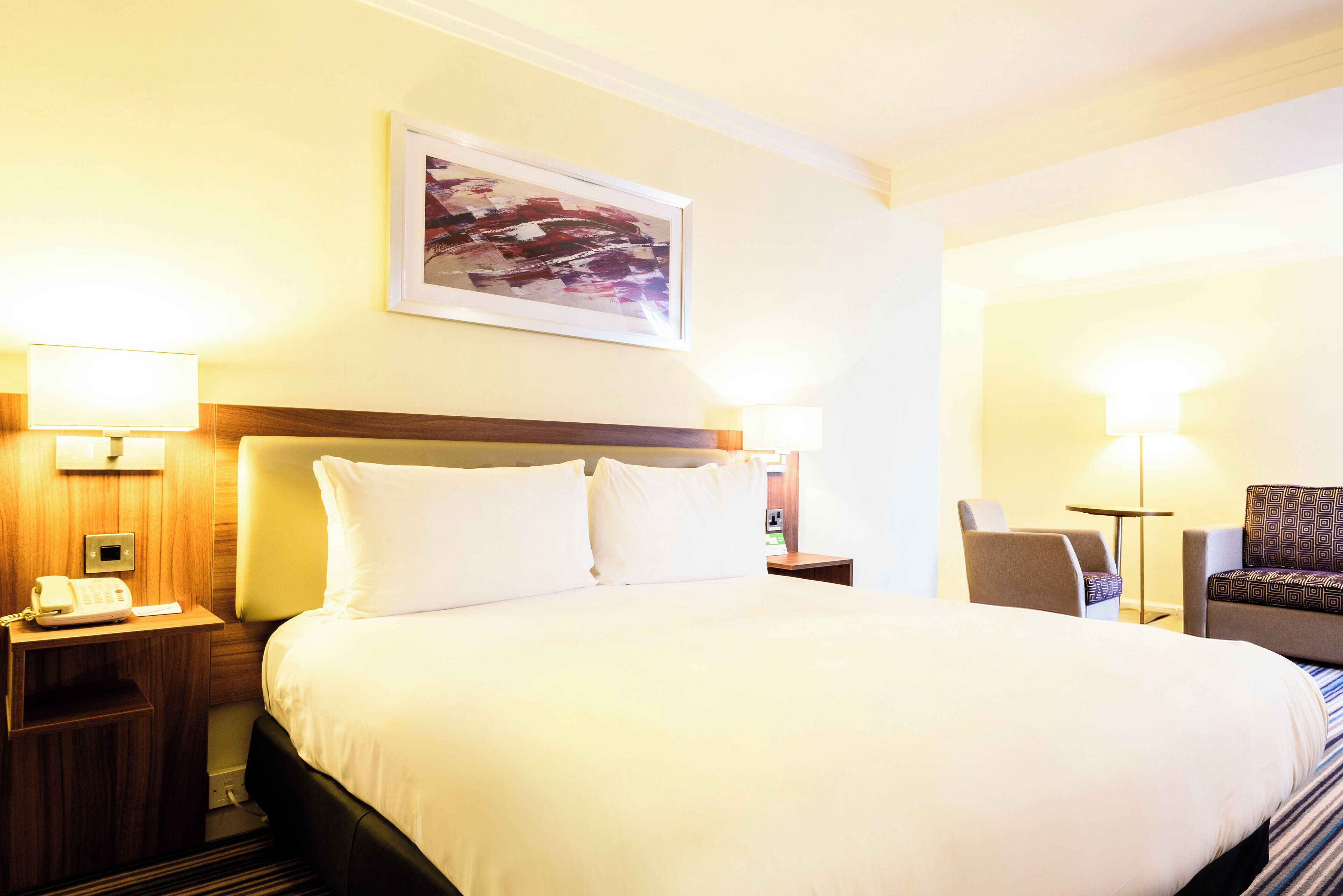 A hotel room with a large bed, two bedside tables with lamps, a chair, and a small table.