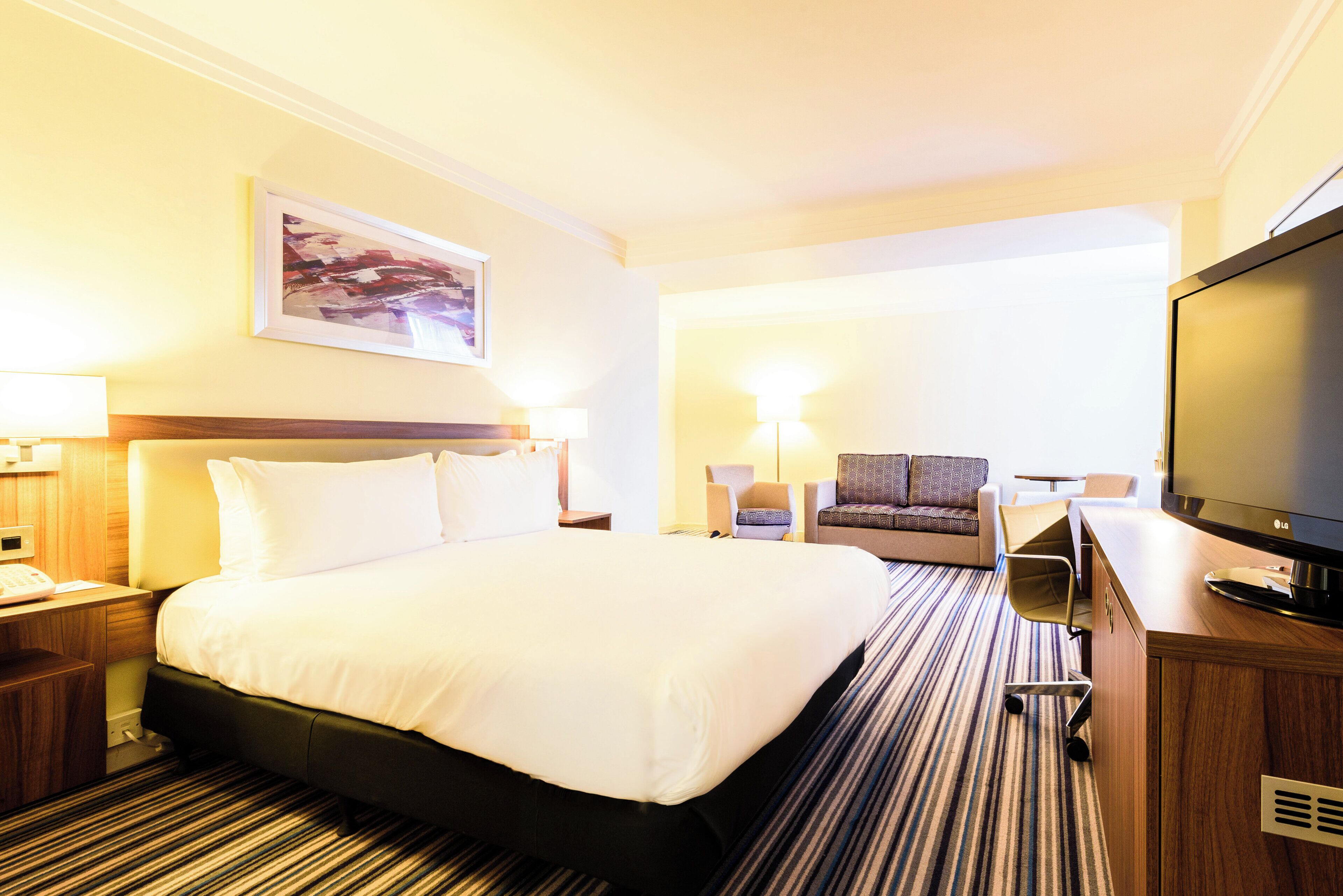 Habitación de hotel con una cama grande, un escritorio con televisor de pantalla plana y una silla.