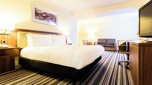 Quarto de hotel com uma cama grande, uma escrivaninha com um computador, uma cadeira e uma televisão.