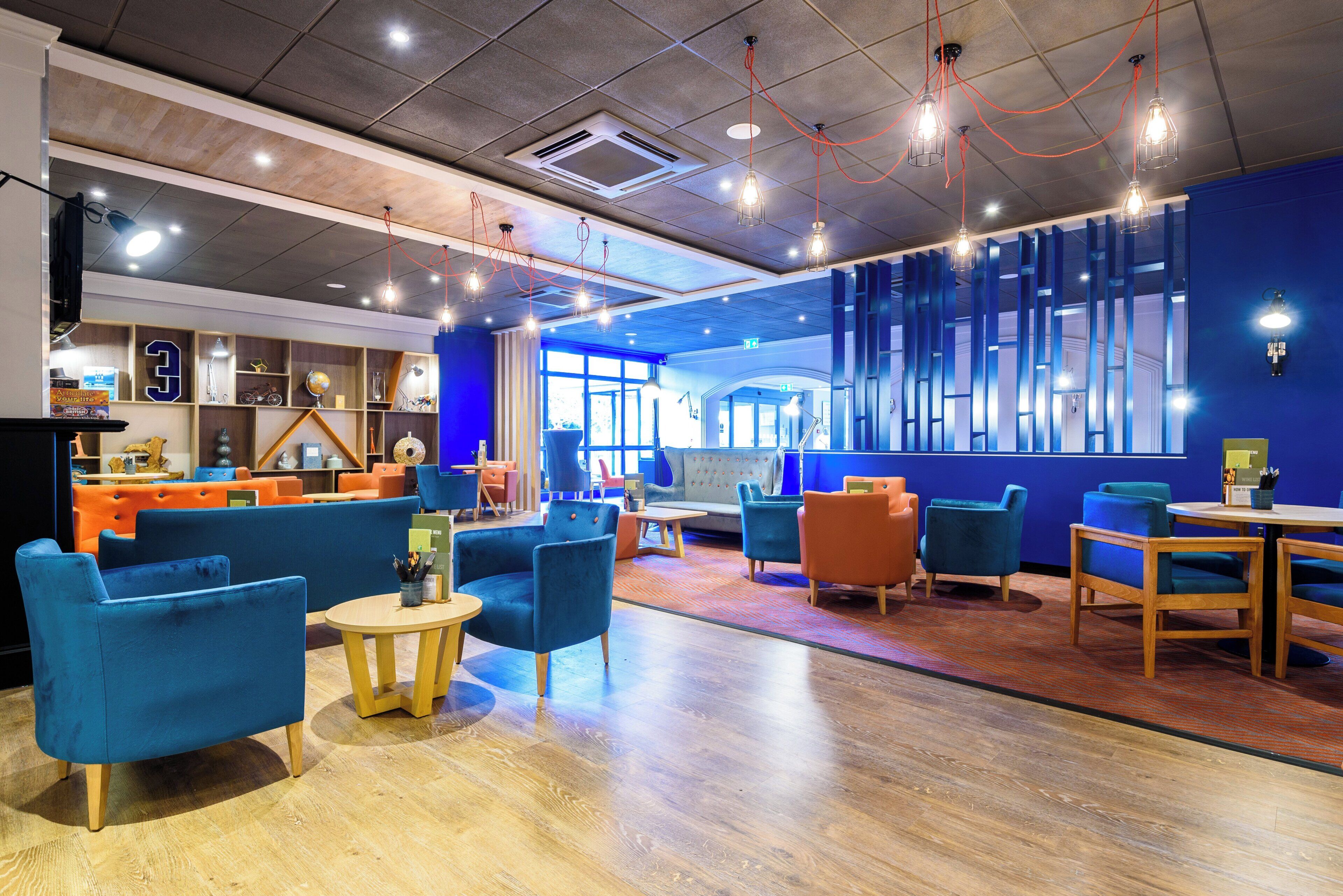 Een moderne zithoek met zitplaatsen, tafels en een blauwe accentmuur.