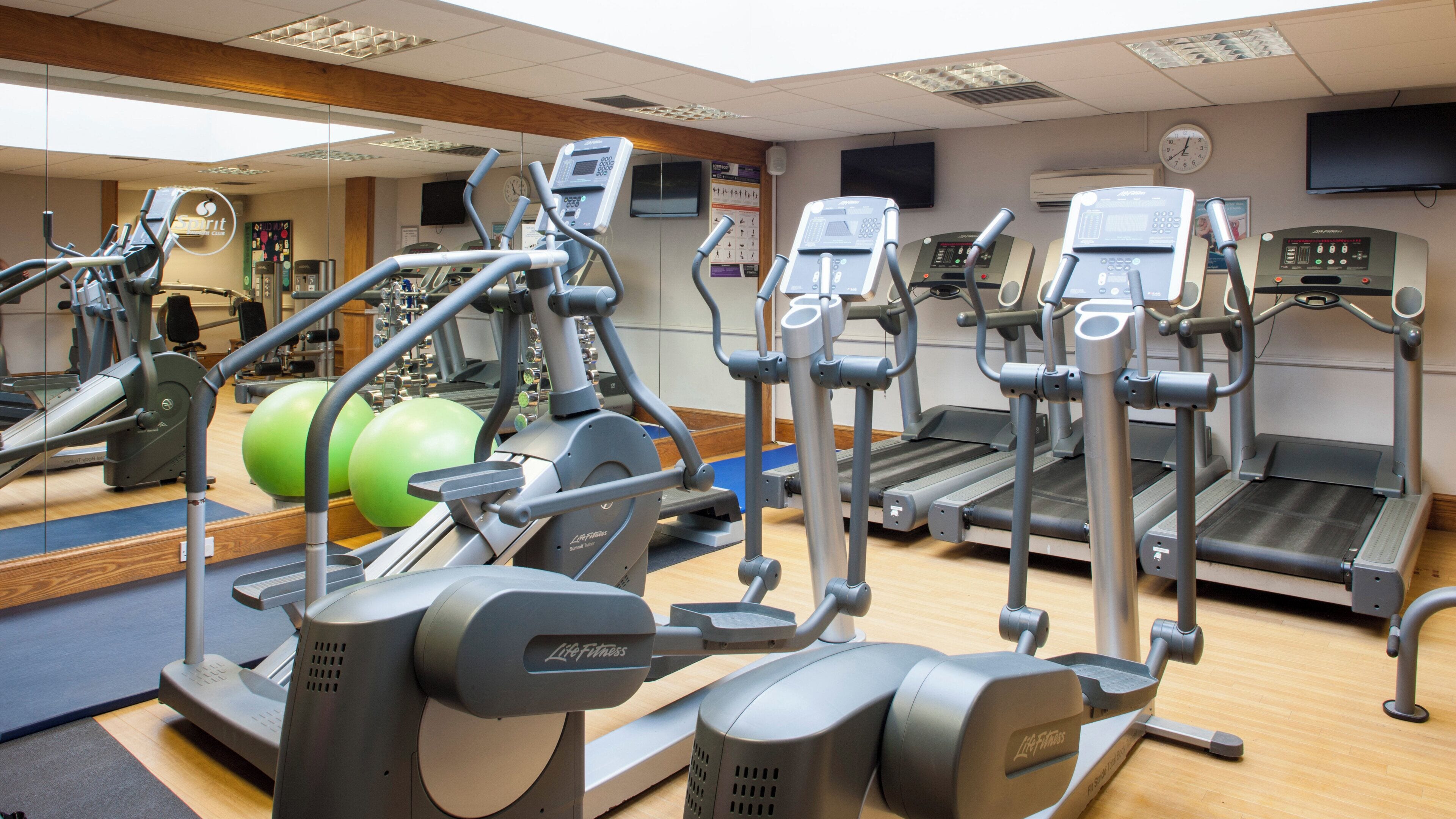 Une salle de sport équipée de divers appareils d’exercice, notamment des tapis de course, des vélos elliptiques et des appareils de musculation.