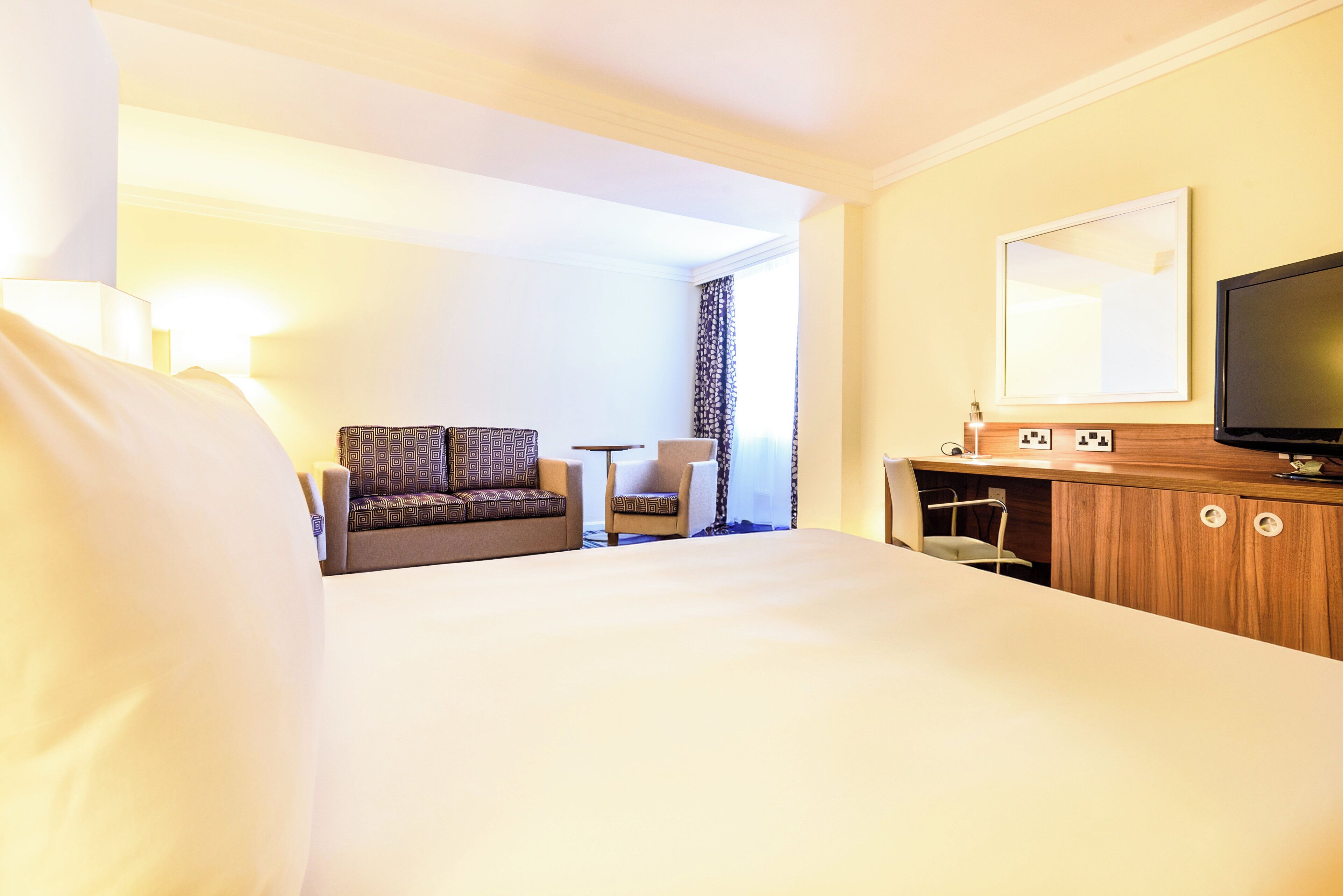 A hotel room with a large bed, a TV, a desk, and a chair.