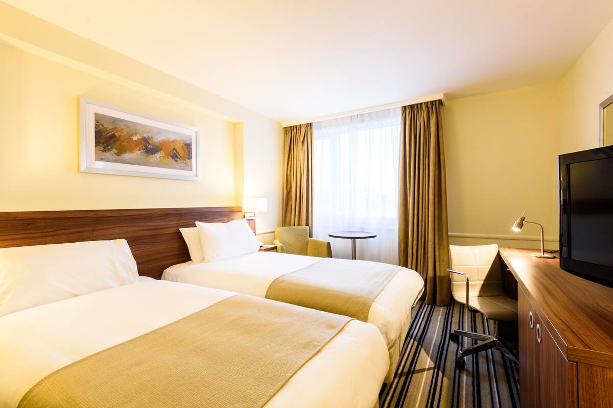 Ein Hotelzimmer mit zwei Betten, einem Schreibtisch, einem Fernseher und einem Bild an der Wand.