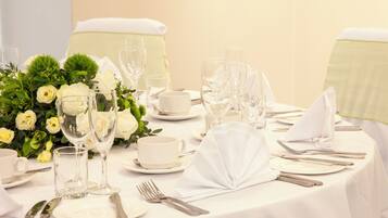 A table set for a formal dining event with white tablecloths, clear glassware, and a floral centerpiece.