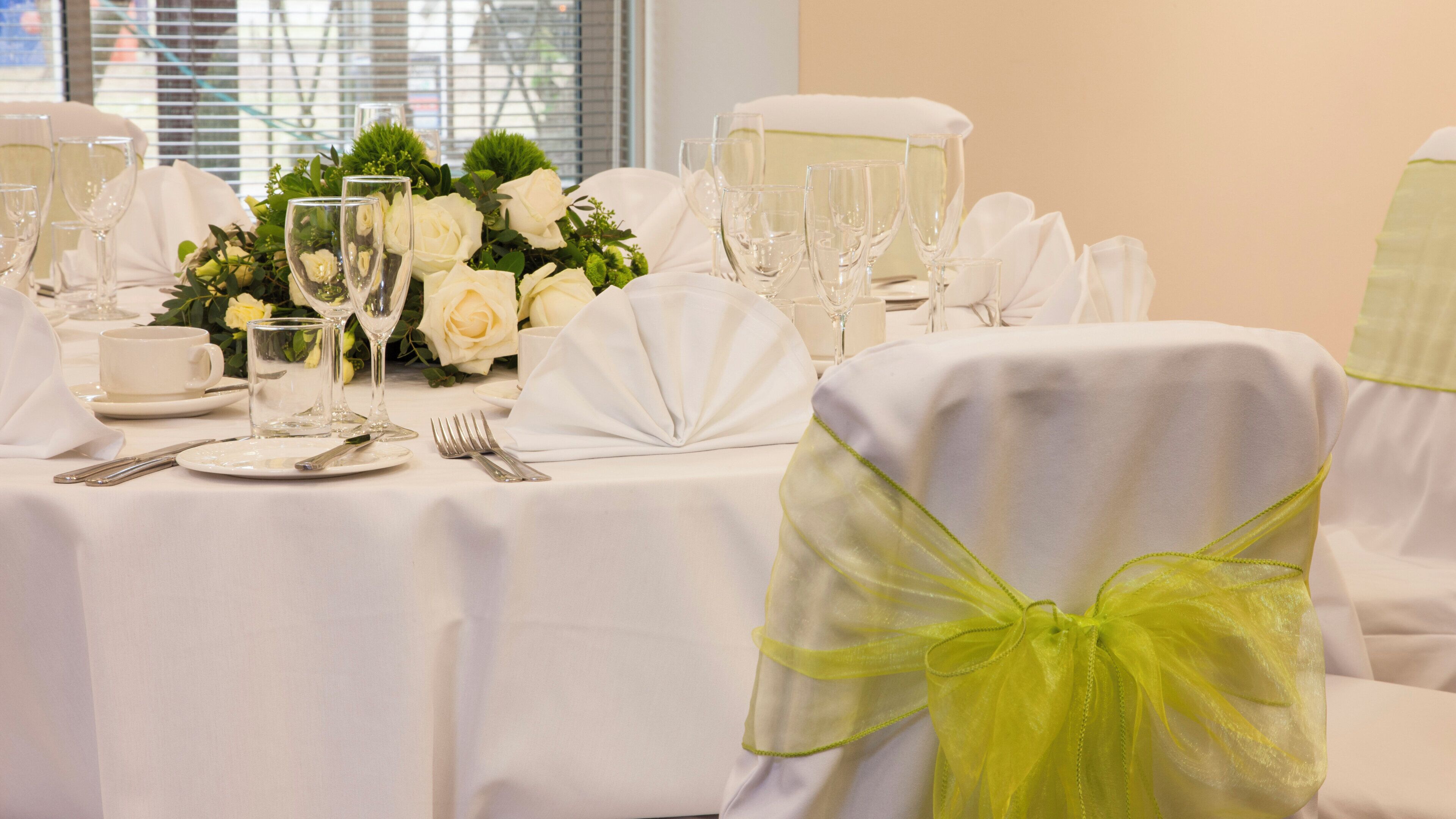 A table set for a formal event with white tablecloths, glassware, and a floral centerpiece.