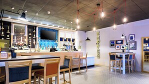 Uma área de bar com cadeiras de madeira, um balcão com garrafas e uma grande tela de televisão.